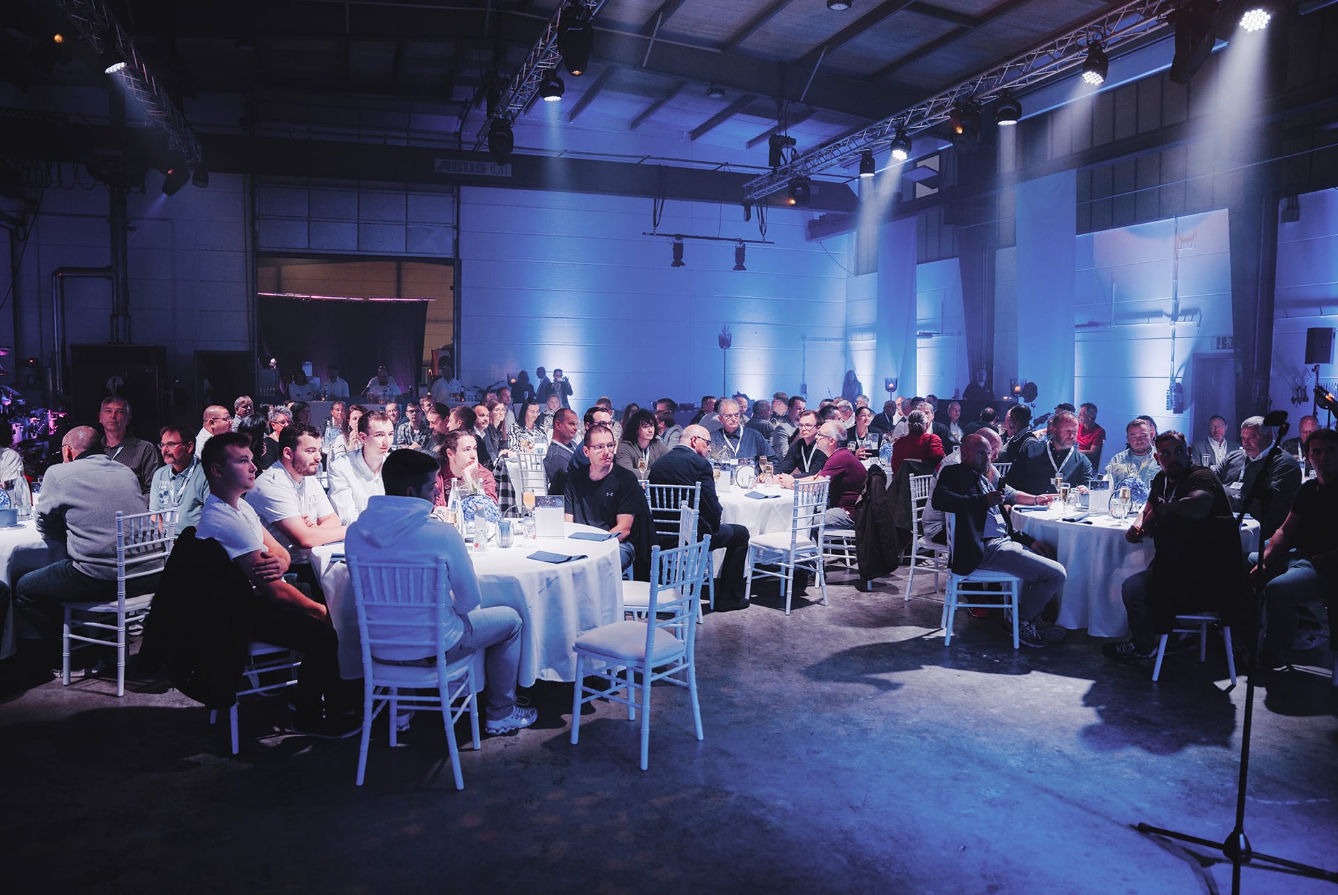 Mitarbeitende der Firma Rotan bei einem feierlichen Firmenevent mit festlich gedeckten Tischen und Bühnenbeleuchtung