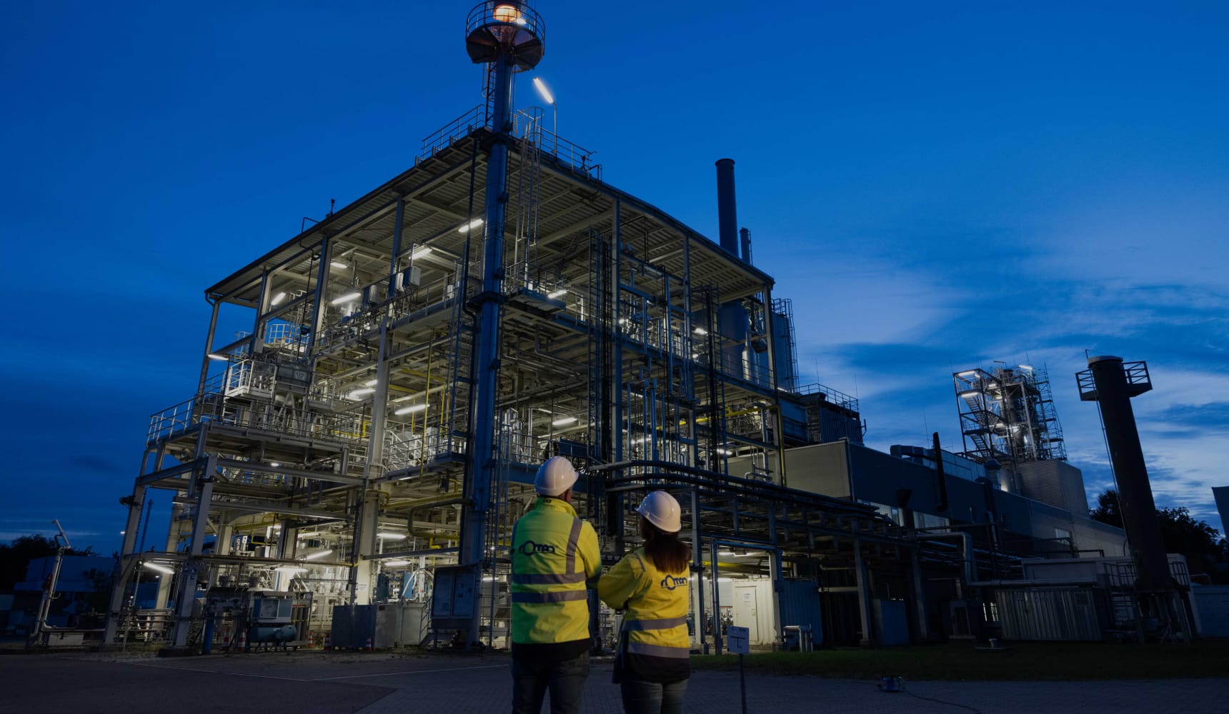 Zwei Mitarbeiter blicken auf eine beleuchtete Industrieanlage bei Nacht